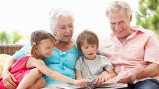 Oma und Opa schauen sich gemeinsam mit ihrer Enkeltochter und ihrem Enkelsohn ein Buch an. Symbolfoto