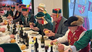 Ministerpräsident Kretschmann sitzt mit Zunftmitgliedern beim Froschkuttelnessen in Riedlingen