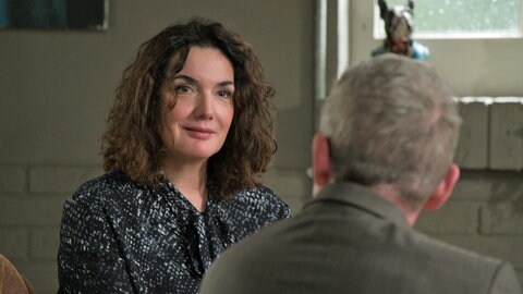 Monique (Anne von Linstow) lächelt Bernhard (Karsten Dörr) an, der im Anschnitt von hinten zu sehen ist.