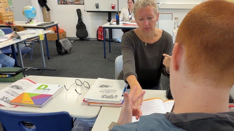 Eine Gebärdendolmetscherin hilft einem Schüler dabei, eine Aufgabe im Unterricht zu verstehen.