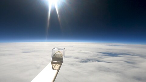 Eine durchsichtige Box mit einem goldenen Ring steht auf einer Holzlatte. Im Hintergrund erkennt man die Stratosphäre. Der Verlobungsring ist 30.000 Meter in die Höhe geflogen.
