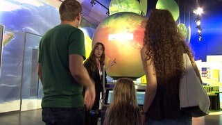 Eine Familie steht in der Klima Arena Sinsheim vor einer vor einer leuchtenden Weltkugel