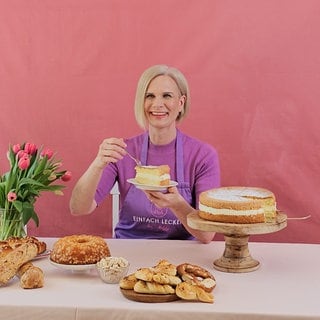 Stefanie Biedermann sitzt in ihrem Studio an einem Tisch. In der einen Hand hält sie einen Teller mit Kuchen und in der anderen ine Gabel.