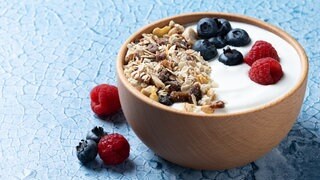 Joghurt mit Nüssen, Müsli, Blaubeeren und Himbeeren in einer Holzschale angerichtet.