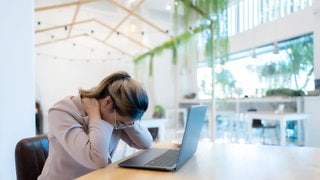 Frau sitzt am Laptop und greift sich in den Nacken 