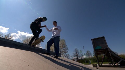 Eine Frau steht auf ihrem Skateboard auf dem Rand einer Rampe. Sie bekommt Hilfestellung von einem Skate-Lehrer. Anja Holz hat mit 38 Jahren angefangen zu skaten.