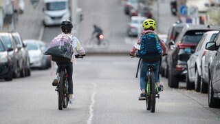Zwei Schulkinder fahren mit ihren Fahrrädern eine Straße entlang. (Symbolbild)