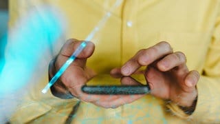 Hände halten ein Smartphone - Lichtreflexe zeigen, dass das Handy gerade mit mobilen Daten genutzt wird.