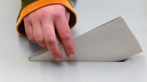 Eine jugendliche Hand steckt einen Stimmzettel in die Wahlurne - in RLP ist Wählen ab 16 bei der Kommunalwahl unzulässig, bei der Europawahl geht's.