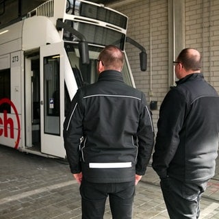 Die Straßenbahnfahrer Marco und Daniel Rungenhagen stehen in einer Halle vor der kaputten Straßenbahn mit der Nummer 273.