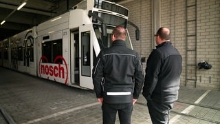 Die Straßenbahnfahrer Marco und Daniel Rungenhagen stehen in einer Halle vor der kaputten Straßenbahn mit der Nummer 273.