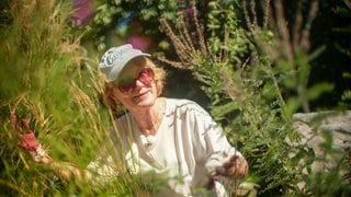 Ute Berninger in ihrem Garten. Sie trägt Sonnenbrille und eine Kappe.