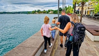 Eine junge Familie ist mit ihren beiden Kindern auf der Uferpromenade in Gardone Riviera, am Westufer des Gardasees, unterwegs.