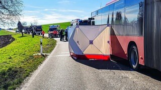 Ein Sichtschutz ist nach einem Unfall an einem Bus zu sehen, während Helfer im Einsatz sind. 
