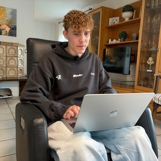 Tom Groß sitzt auf einem Sessel an seinem Laptop.