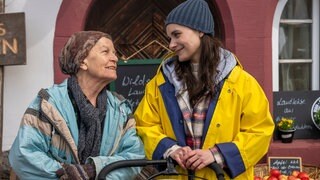 Lioba (Lisbeth Felder) und Jenny (Julia Obst) stehen hinterm Hofladen und lächeln sich an