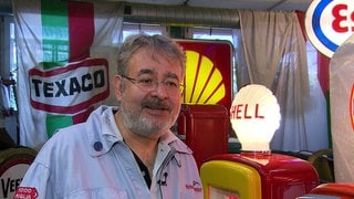 Arno Saager aus Ludwigsburg sammelt historische Tanksäulen. Er steht zwischen Tanksäulen und Tankstellenfahnen.