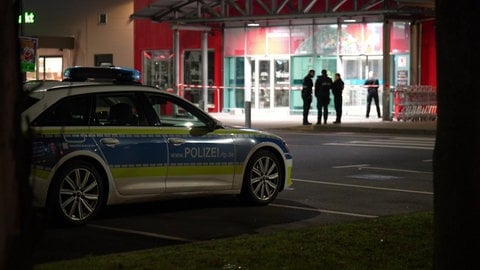 In der Nacht stehen Polizisten vor dem Eingang des Einkaufsmarktes und sichern ihn ab. 