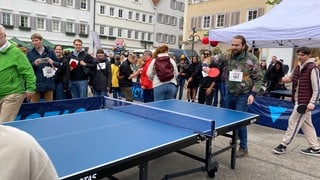 Ein Mann steht an einer Tischtennisplatte und schlägt den Ball über's Netz. Er ist ein Teilnehmer beim Weltrekordversuch im "Mäxle-Tischtennisspiel in Reutlingen.