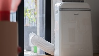 Ein mobiles Klimagerät mit Abluftschlauch zur Balkontür steht in einer Neubauwohnung