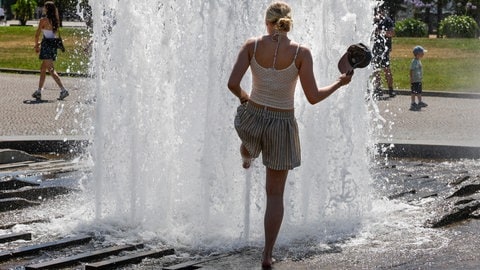 Eine frau mit kurzer Hose kühlt sich an einer Springbrunnenfontäne in der Hitze die Füße