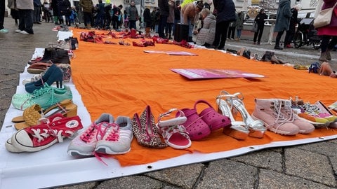 Nahaufnahme von einigen Schuhpaaren, die zusammen auf dem Marktplatz in Biberach die Zahl 155 bilden. Eine Aktion der Bewegung One Billion Rising.
