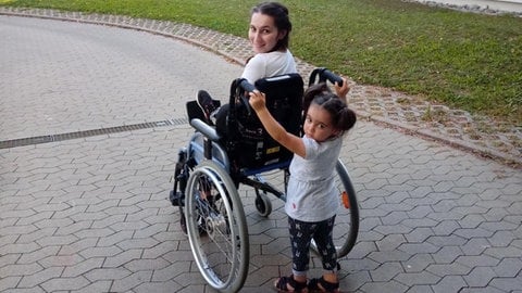 Ein kleines Mädchen schiebt eine junge Frau, die in einem Rollstuhl sitzt. In unserer Reihe "SWR1 Neuanfang" portraitieren wir Luana: Sie hat einen Raserunfall überlebt, ihr Mann und ihr Baby starben. Trotz des großen Traumas kämpfte sie sich zurück ins Leben.