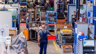 Ein Mitarbeiter geht im DB Fahrzeuginstandhaltung Werk mit einer roten Transportkiste durch die Halle. 