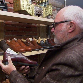 Ein Kunde steht in einem Second Hand-Schugeschäft und schatet sich verschiedene Lederschuhe an.