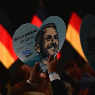 Ein Schild in Herzform mit dem Porträt von AfD-Spitzenkandidat Siegmund ist bei der Wahlparty der AfD. Das Erstarken der AfD im Osten wirkt sich auch auf Baden-Württemberg aus: Forschende warnen vor mehr Polarisierung, die Zivilgesellschaft hofft und bangt zugleich.