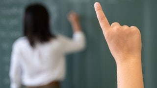 Schüler meldet sich, im Hintergrund Lehrkraft an einer Tafel