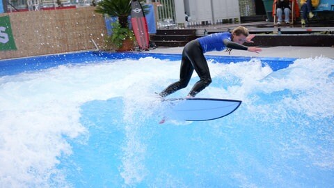 Eine surferin springt mit ihrem Brett in einer känstlichen Welle.