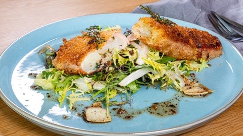 Spargel umwickelt mit Schinken und Käse und lecker paniert liegt auf einem Salatbett auf einem Teller.