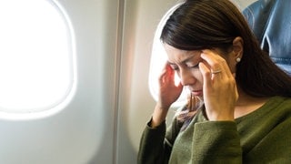 Frau im Flugzeuig auf ihrem Sitz leidet unter Flugangst | So lässt sich Flugangst überwinden