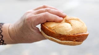 Eine Hand hält ein Brötchen mit Fleischkäse - Polizei ermittelt gegen Frau, die Fleischkäse-Brötchen in Kaiserslautern gestohlen haben soll