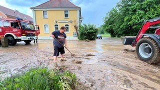 Wegen des Starkregens wurden Schlamm und Geröll durch die Straßen Binaus (Neckar-Odenwald-Kreis) gespült. Ein Mann hilft bei den Säuberungsarbeiten.