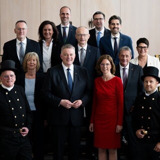 Gruppenfoto der RLP-Regierung mit den 10 Ministern und Ministerinnen, Ministerpräsident Gordon Schnieder und zwei Schornsteinfegern.