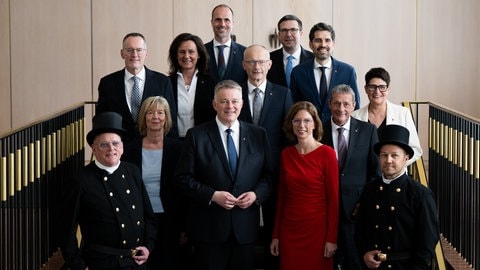 Gruppenfoto der RLP-Regierung mit den 10 Ministern und Ministerinnen, Ministerpräsident Gordon Schnieder und zwei Schornsteinfegern.
