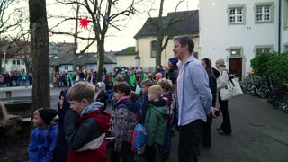 Sebastian Heinricht, der junge Schulleiter einer Grundschule steht mit vielen Kindern auf dem Pausenhof. 