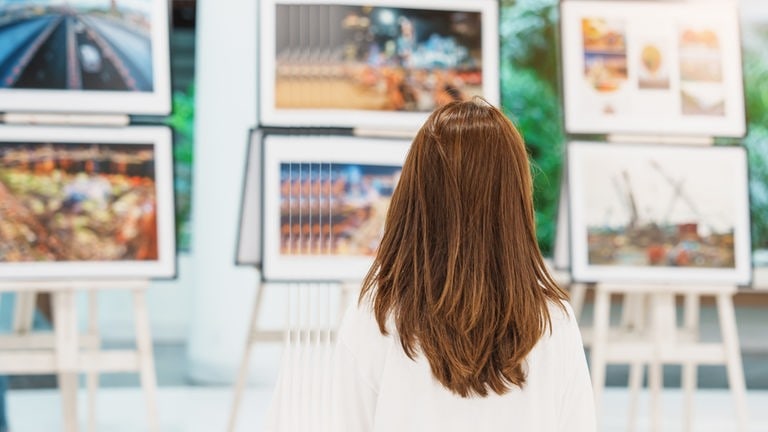 Eine Frau mit braunen langen Haaren steht vor mehreren Staffeleien mit Bilder