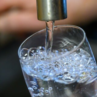 Trinkwasser läuft aus einem Wasserhahn in ein Glas.