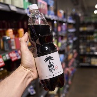 Eine Hand hält eine Flasche afri cola in einem Supermarkt