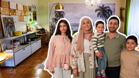 Ayşe steht mit ihrem Mann und ihren drei Kindern in ihrem Wonhzimmer, das sie in einem Stilmix aus großen Prints, alten Lampen und bunten Farben eingerichtet hat.