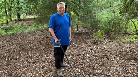 Sondengänger steht im Wald und hält seinen Metalldetektor in der Hand