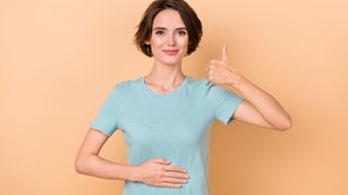Frau hält sich den Bauch, Daumen nach oben