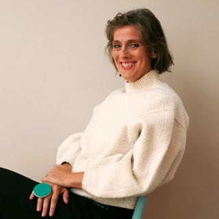 Autorin Katrin Wilkens sitzt auf einem Stuhl und lacht in die Kamera.
