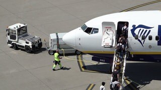 Ein Flugzeug steht auf dem Rollfeld des Flughafens Baden-BadenKarlsruhe. Passagiere steigen ein, links hinter dem Flugzeug sieht man den Kofferwagen.