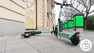 Zwei grüne E-Scooter blockieren einen Gehweg. Der eine liegt auf dem Gehweg. Der andere steht aufrecht. Rechts das SWR Logo für Leichte Sprache.  
