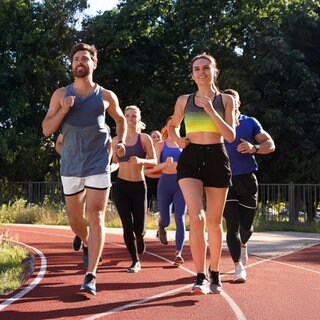 Gruppe von Läufern auf einer Tartanbahn: Laufclubs boomen, immer mehr Menschen trainieren für einen Marathon. Regelmäßiges Laufen stärkt das Herz-Kreislauf-System und hilft, Stress abzubauen – auch ohne extreme Distanz.