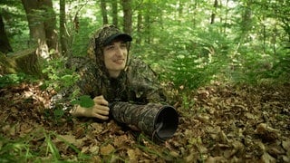 Junger Mann mit Tarnkleidung im Wald liegend